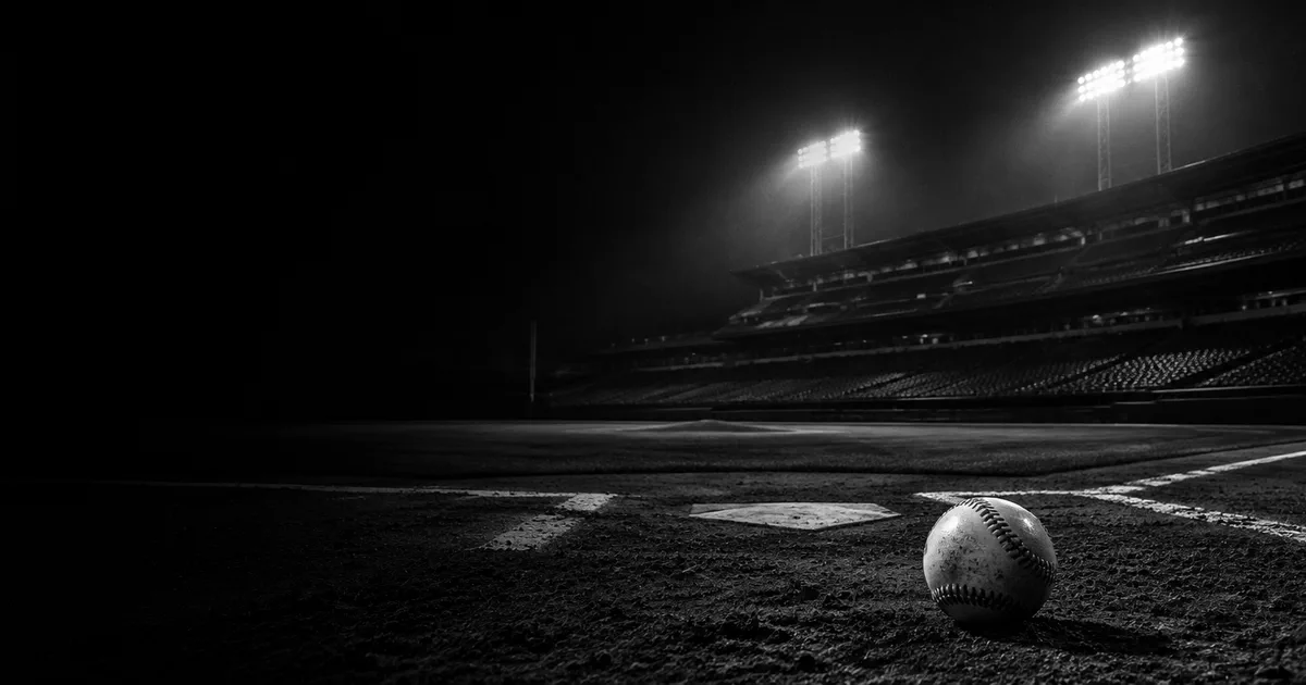 A single baseball on the infield dirt of an empty stadium at night, under floodlights