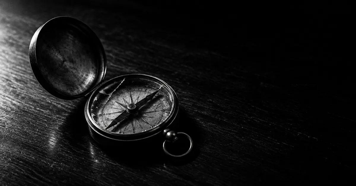 An old brass pocket compass with cracked glass lying open on a dark wooden desk, lit from the side